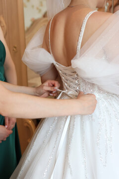 Hands tighten the lacing on the back of the bride&rsquo;s wedding dress; ceremony preparation and tender wedding shot.