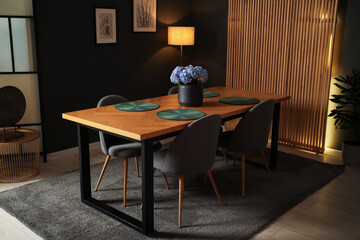 Wooden table with beautiful flowers and chairs in dining room at night