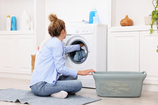 Woman putting dirty laundry into washing machine indoors - Powered by Adobe