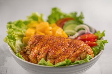 Fototapeta premium Spiced chicken salad featuring lettuce, mango, red bell pepper, and cucumber with a focus on the foreground meat