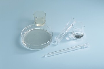 A collection of Petri dishes with a pipette and glass container on a blue surface