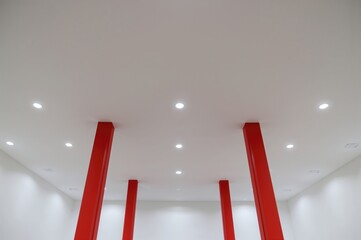 Contemporary ceiling design with embedded lights and striking red columns set against pristine white walls, showcasing a symmetrical and minimalist bright interior.