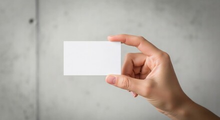 Fototapeta premium Clean White Business Card Held By A Hand In Front Of A Textured Concrete Wall Background