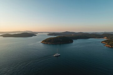 Gentle radiance bathes a peaceful cluster of wooded islets with a solitary vessel navigating serene waters, highlighting the expansive sky and ocean.