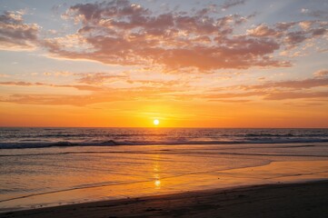 Evening sky with golden sunlight casting over the ocean and sandy shore, summer twilight with vibrant orange and yellow clouds