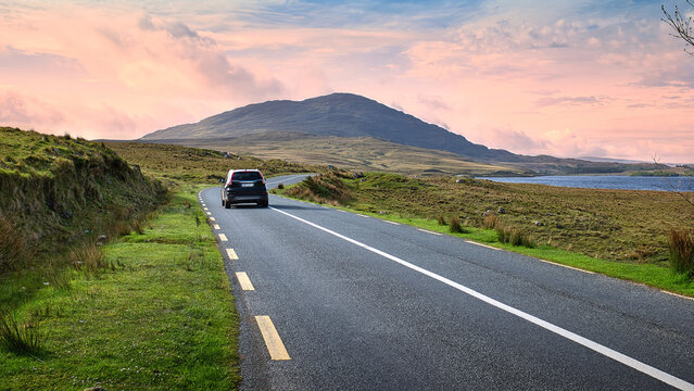 Car driving on scenic country road in Connemara Ireland with mountains and lake at colorful sunset sky, nature background - Powered by Adobe