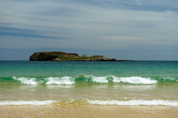 Scenic view of the turquoise Atlantic Ocean and a small rocky island near the Sagres coastline, sunny weather and calm waves.