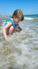 Happy little girl having fun in sea waves. Smiling girl enjoying the sea water, getting splashed by sea foam.