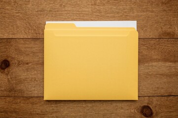 Top-down view of a yellow folder containing papers on a wooden surface with room for text