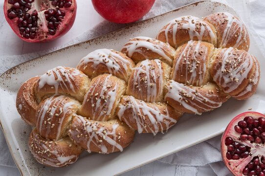 Traditional braided bread topped with white glaze, pomegranate, and sesame seeds in Jewish cooking