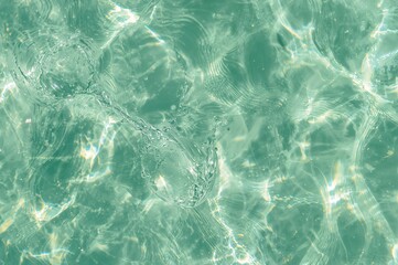 Obraz premium Clear green water surface with ripples and splashes, abstract natural background with sunlight reflections, top-down view
