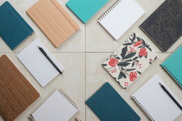 Flatlay of assorted notebooks and notepads on a tiled surface viewed from above