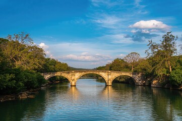 Fototapeta premium Bridge spanning the Obsha River under a clear blue sky with lush green shores