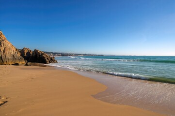 Fototapeta premium Sunny day by the ocean with waves crashing over coastal rocks