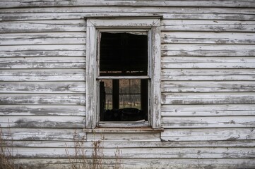 Rustic deserted home featuring shattered glass window and aged white wooden exterior.