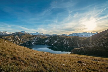 Discover the magical charm of mountain scenery at the peak of summer, featuring a serene lake surrounded by snowy hills beneath a vast sky