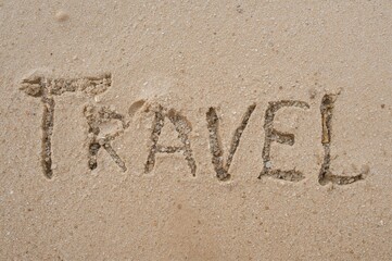 Fototapeta premium Alphabet of the word 'travel' etched in golden sand on a sunny beach