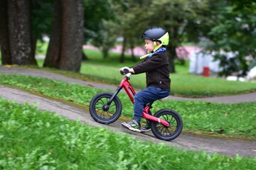Young boy riding balance bike with helmet on curved asphalt track. Child enjoys sport activity, balancing carefully while cycling outdoors on pump track in autumn season.