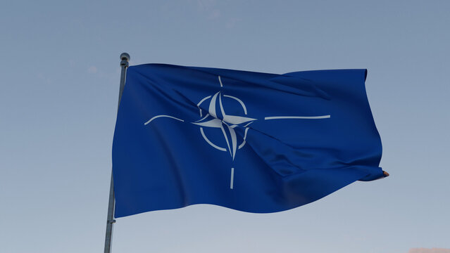 Waving NATO flag with white compass emblem on a blue background against clear sky, symbolizing security, defense, unity, and international military alliance.