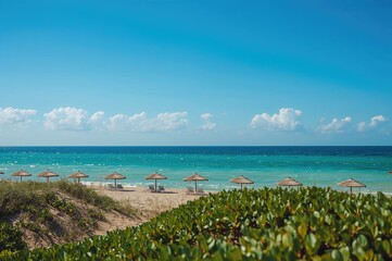 Obraz premium Sunlit sandy shore with woven parasols under clear azure sky and ocean - focused detail