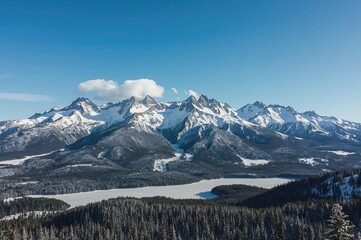 Snow-capped peaks under a clear sky with a forested winter landscape