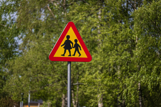 Children crossing triangular warning sign on roadside.