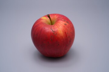 Single red apple with yellow and green hues on a neutral background