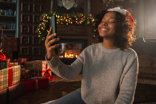 Merry Christmas. African woman in Santa hat having video chat in smartphone. Blogger in festive mood recording video in social network. Girl having video call with friends family celebrating Christmas