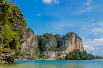 Fototapeta premium Cliffs, palm trees and sandy beach in Krabi, Thailand, with turquoise sea, limestone formations, and tropical vegetation under clear sky, showing coastal landscape travel destination in Andaman sea