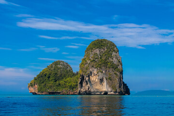 Fototapeta premium Cliffs, palm trees and sandy beach in Krabi, Thailand, with turquoise sea, limestone formations, and tropical vegetation under clear sky, showing coastal landscape travel destination in Andaman sea