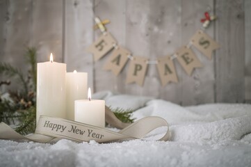 Holiday white candles with New Year's greeting ribbon on a snowy wooden surface