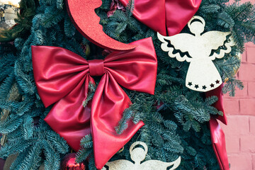 Close-up of a decorated Christmas tree with a large red bow, glittering gold angel decorations, and festive evergreen branches in traditional holiday style