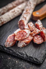 Sliced fuet sausage with mold on black cutting board.