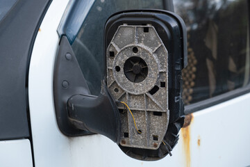 Detailed view of a damaged side mirror housing on an old vehicle, with missing glass and visible inner wires. Symbol of wear, neglect, or vandalism