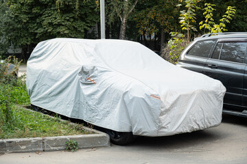 A car parked on a city street under a full protective cover, symbolizing personal property care, privacy, and urban infrastructure.