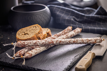 Fuet sausage with mold on black cutting board.