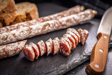 Sliced fuet sausage with mold on black cutting board.