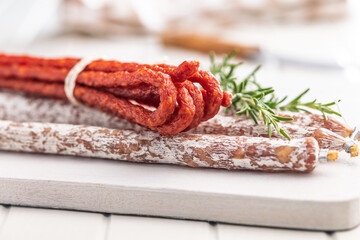 Fuet sausage with mold and smoked kabanos mini salami on white cutting board.