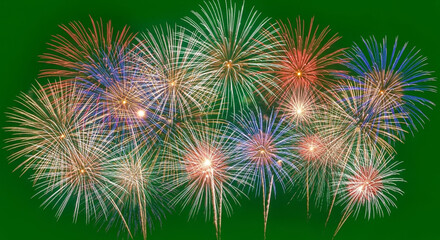 Vibrant fireworks explode in a dazzling display of color across a deep green night sky