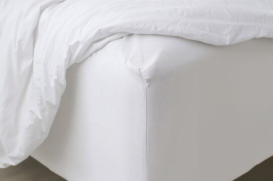 Corner of bed with white elastic fitted sheet