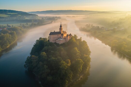 Bird's-eye view of a fog-covered terrain featuring an ancient hilltop fortress by a flowing river in the eastern region of Bohemia.