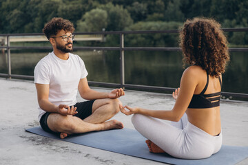 Young couple meditating outdoors on yoga mat