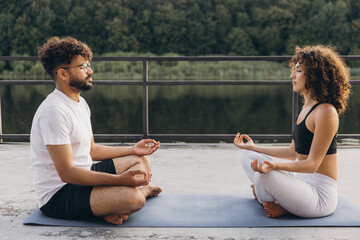 Couple meditating outdoors practicing yoga on a mat by the lake