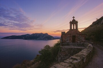 Sunset view of a mountain landscape with sea and historic religious building in the background