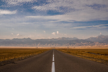 Fototapeta premium The road goes over the horizon. A conceptual symmetrical landscape, the highway goes forward and disappears into the distance. Steppe and mountains on the horizon, there are no people