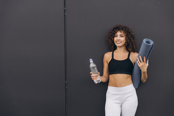 Young sporty woman holding yoga mat and water bottle