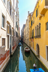 Quiet narrow canal with boats in Venice. Colorful historic buildings line a peaceful Venetian canal, where small boats float on still water under a sunny blue sky.