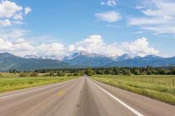 Fototapeta premium A road extends into scenic mountain peaks beneath a clear blue sky dotted with clouds, bordered by lush green meadows.