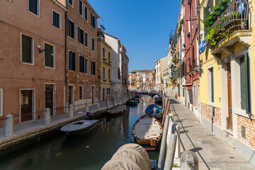 Quiet residential canal with boats in Venice. Small boats line a calm canal in a peaceful residential area of Venice, with colorful buildings and clear blue skies above.