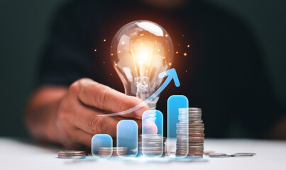 Innovation and financial growth concept. Businessman hand holding a glowing light bulb with stacked...